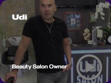 A person stands in a beauty salon, leaning on a chair. The salon features "Udi" branding prominently on the counter.