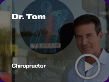 A person stands near a glass window displaying a chiropractic logo. Text reads "Dr. Tom Chiropractor" with a play button symbol present.