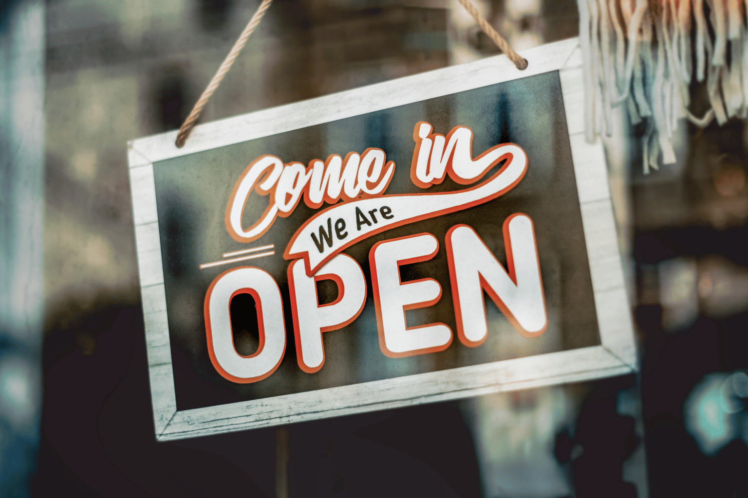 A storefront window sign reading “Come in, We are OPEN” hanging in a glass door.