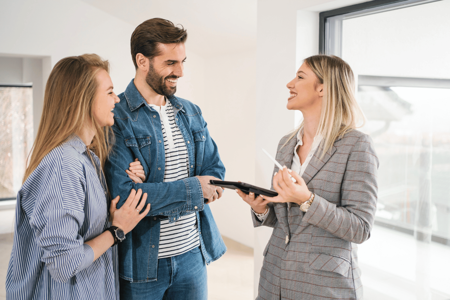 Three coworkers in a bright office discuss a tablet, smiling at each other.